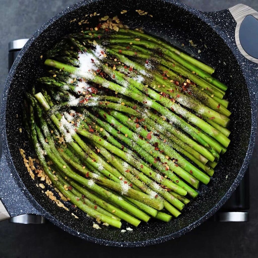 A pan with Sauteed Asparagus and sprinkled seasonings.
