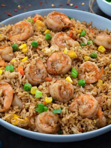 Shrimp Fried Rice in a white plate with few ingredients scattered around.