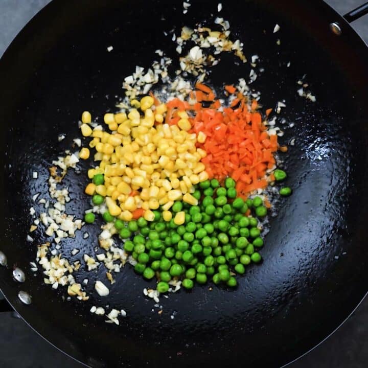 A wok with veggies and aromatics.