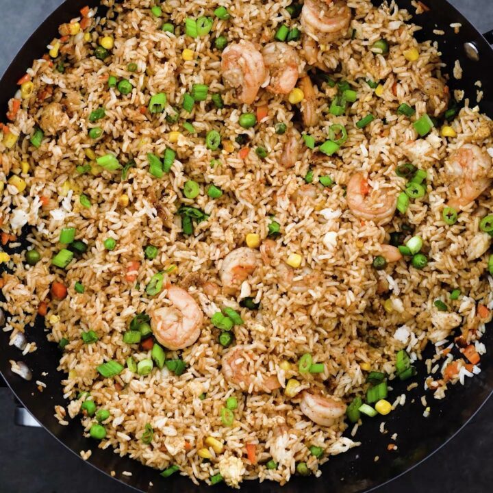 A wok with shrimp fried rice that is garnished with spring onions.
