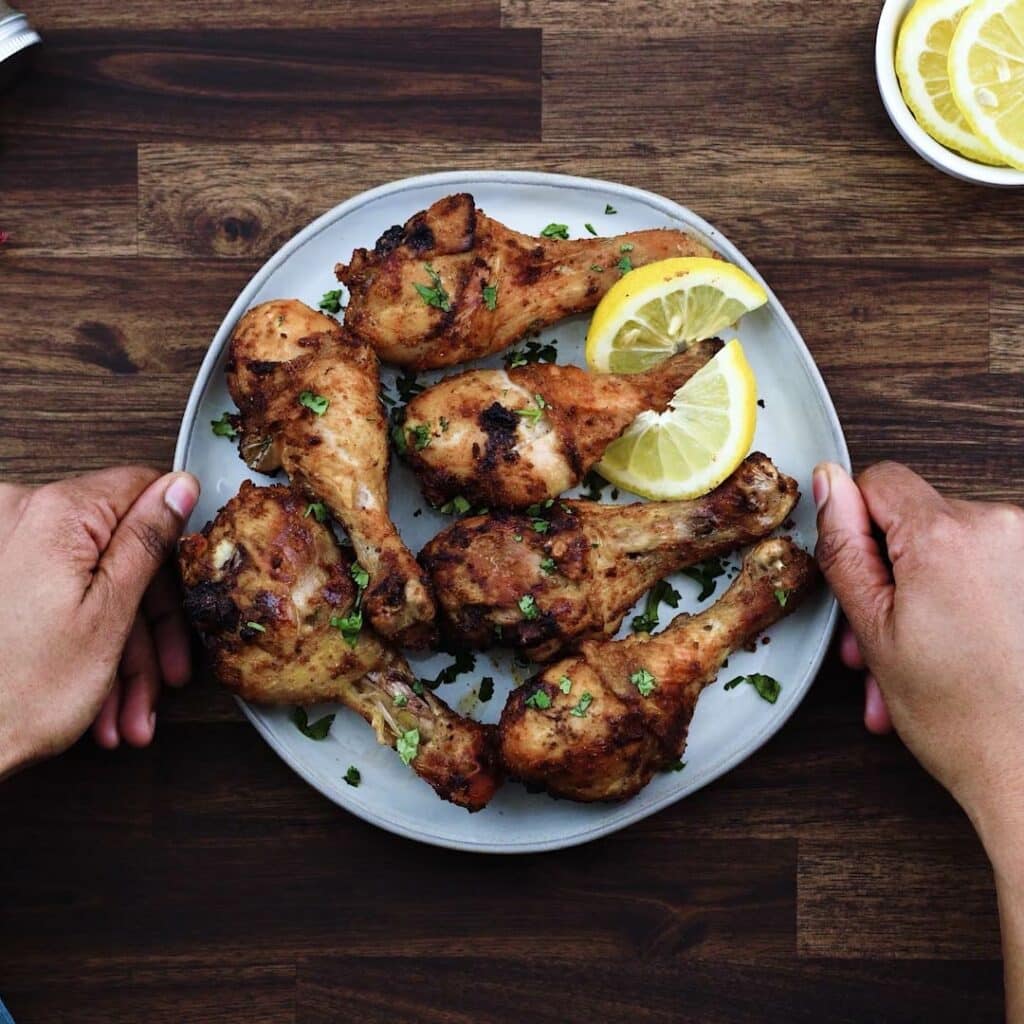 Serving air fryer chicken legs in a white plate with lemon slices.