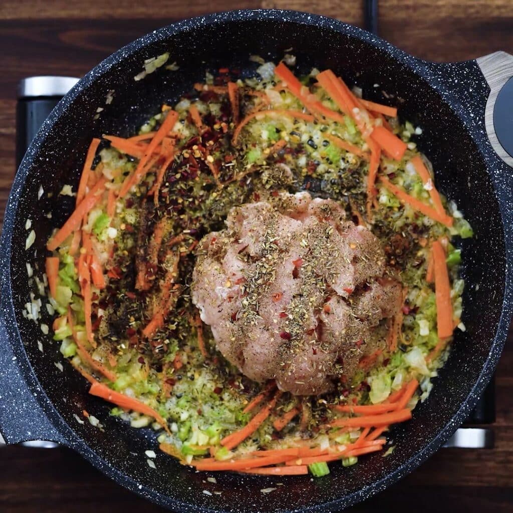 A pan with veggies, boneless chicken and seasonings.