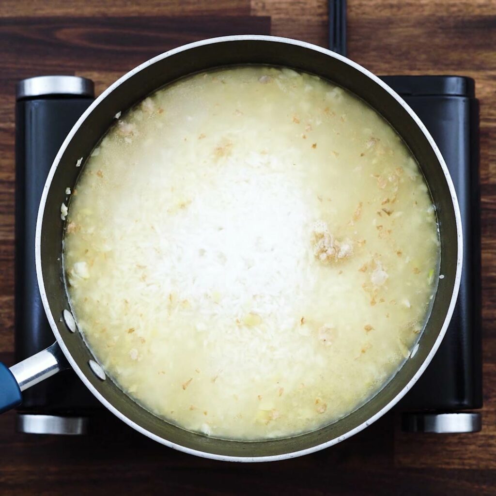 A pan with rice cooking in a chicken broth.