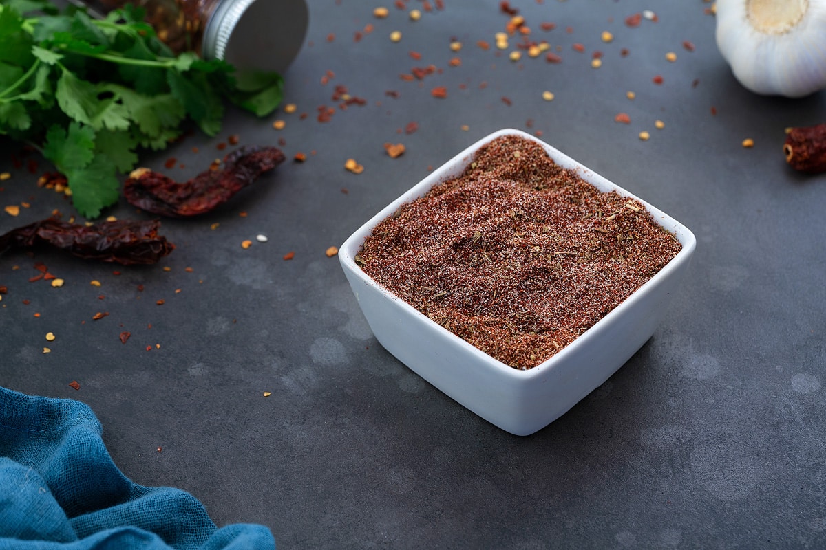 Homemade Blackened Seasoning in white squre bowl with few ingredients scattered around.