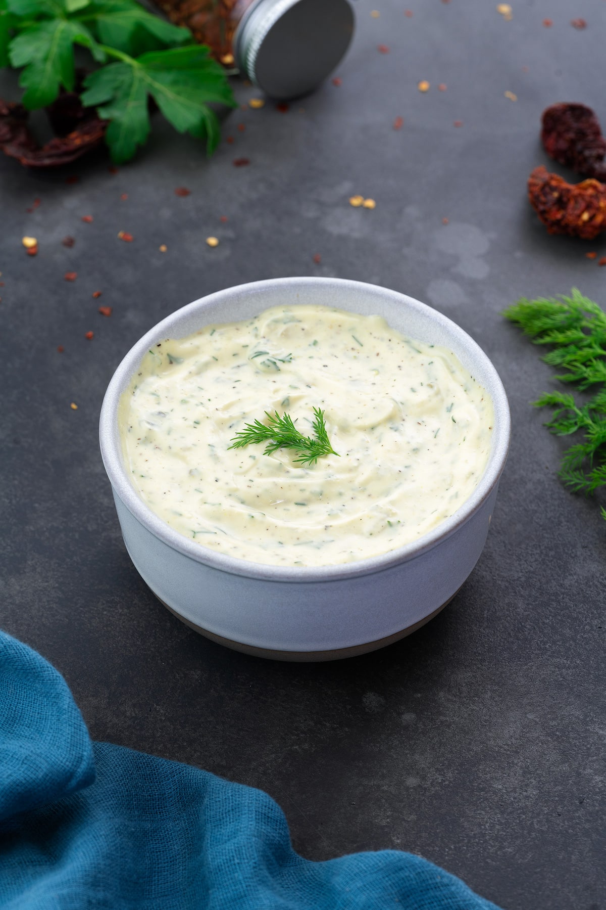 Homemade Tartar Sauce in a white bowl with few ingredients scattered around.