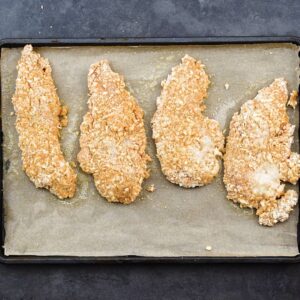 A baking tray with breaded chicken tenders.