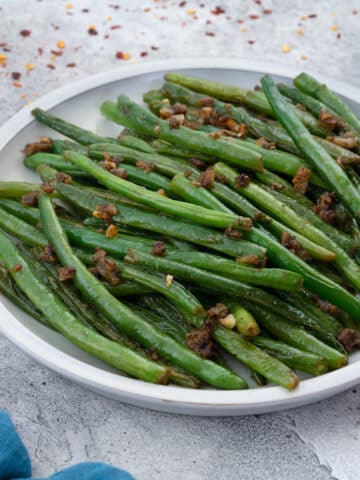 Sauteed Green Beans in a white plate with few ingredients scattered around.