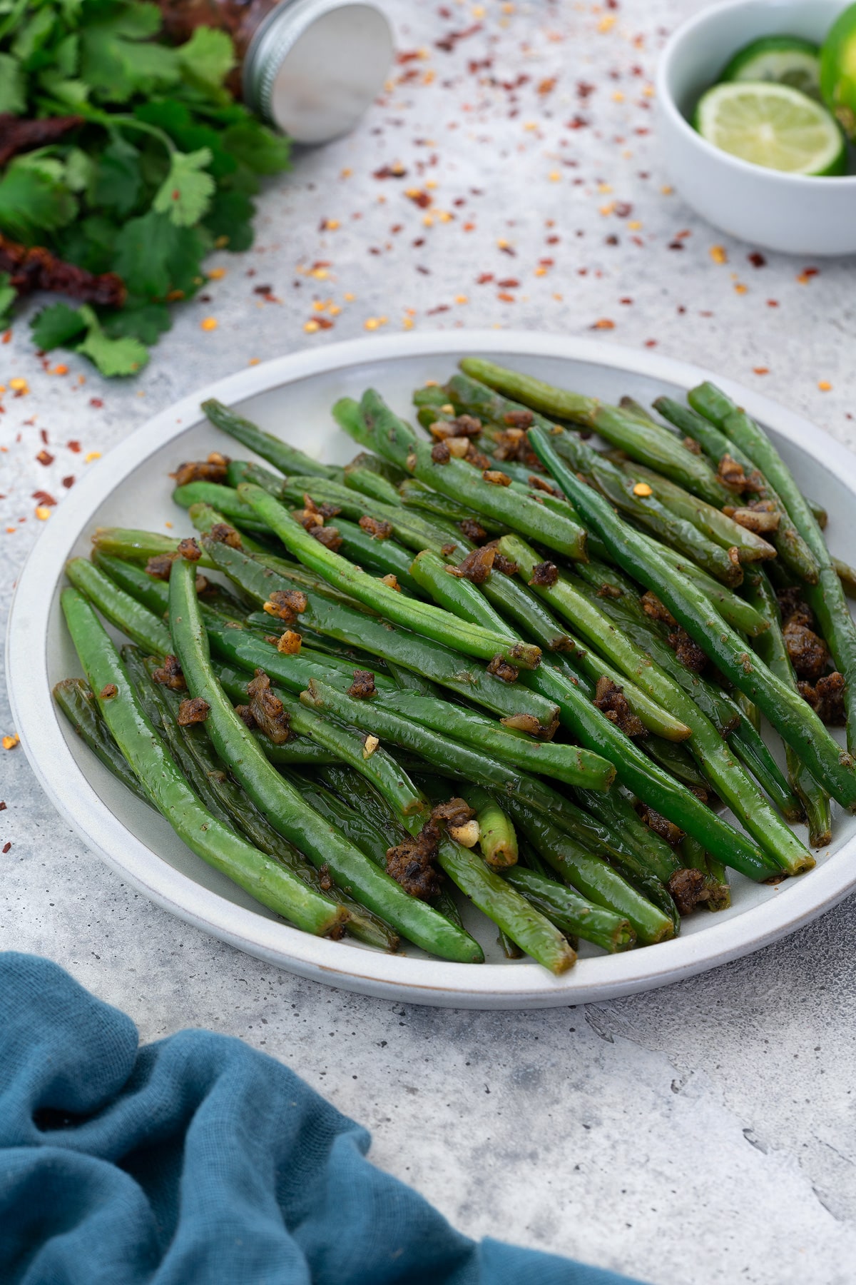 Sauteed Green Beans in a white plate with few ingredients scattered around.