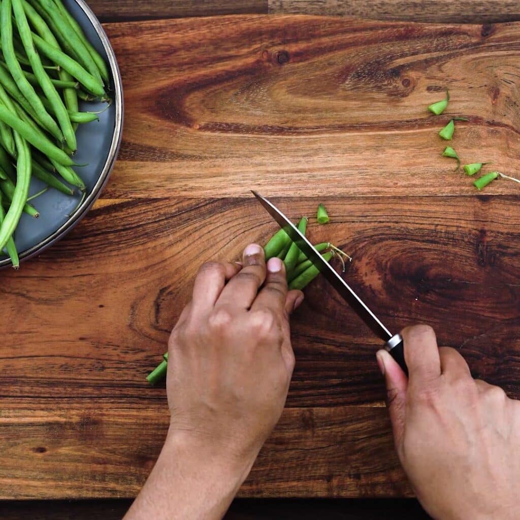 Trimming the green beans using a kitchen knife.