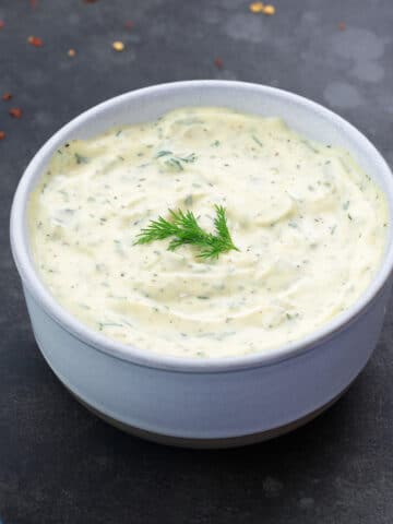 Homemade Tartar Sauce in a white bowl with few ingredients scattered around.