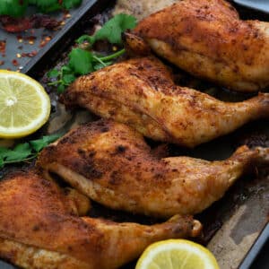 Oven Baked Chicken Leg Quarters in a baking tray with lemon slices and greens.