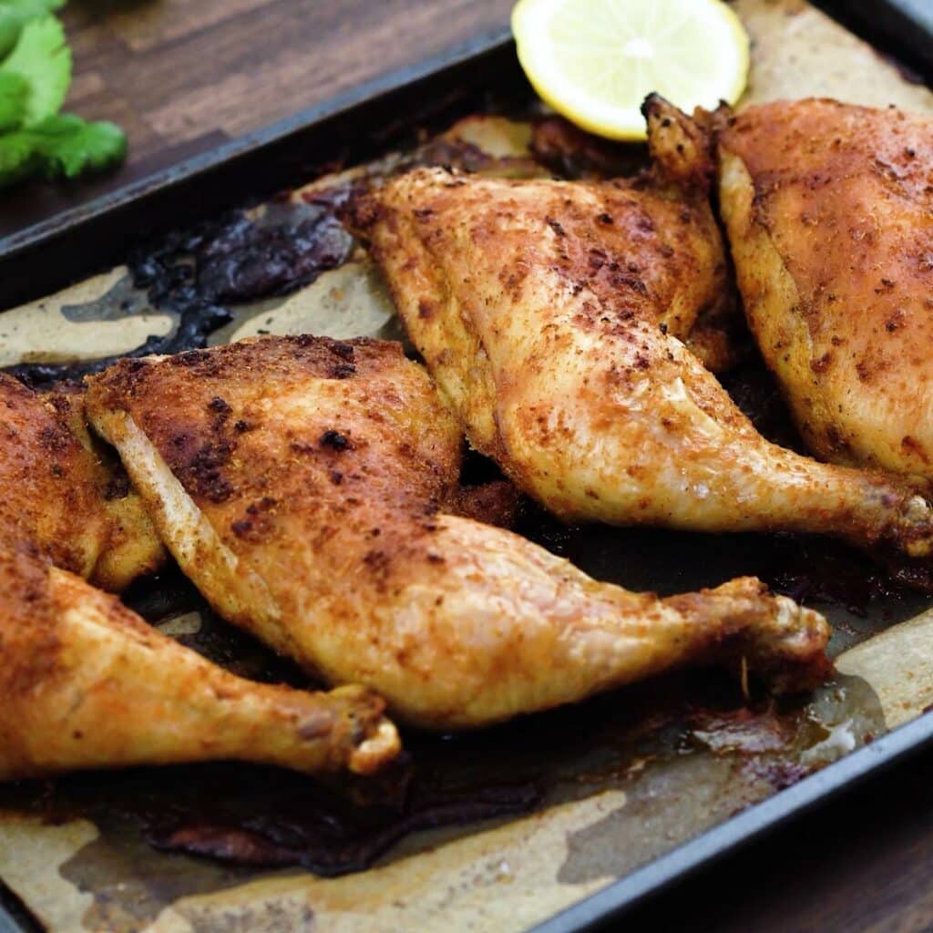 Chicken leg quarters served in a tray with lemon slices and cilantro leaves.