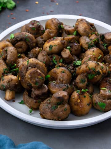 Garlic Mushrooms served in a white plate on a grey table.