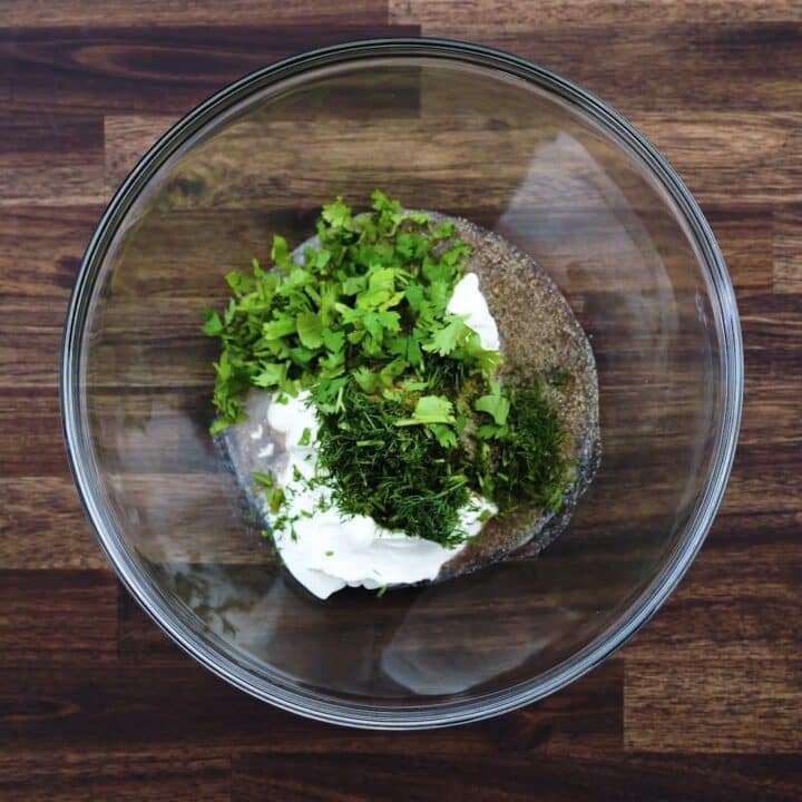 A bowl with sour cream, herbs and seasonings.