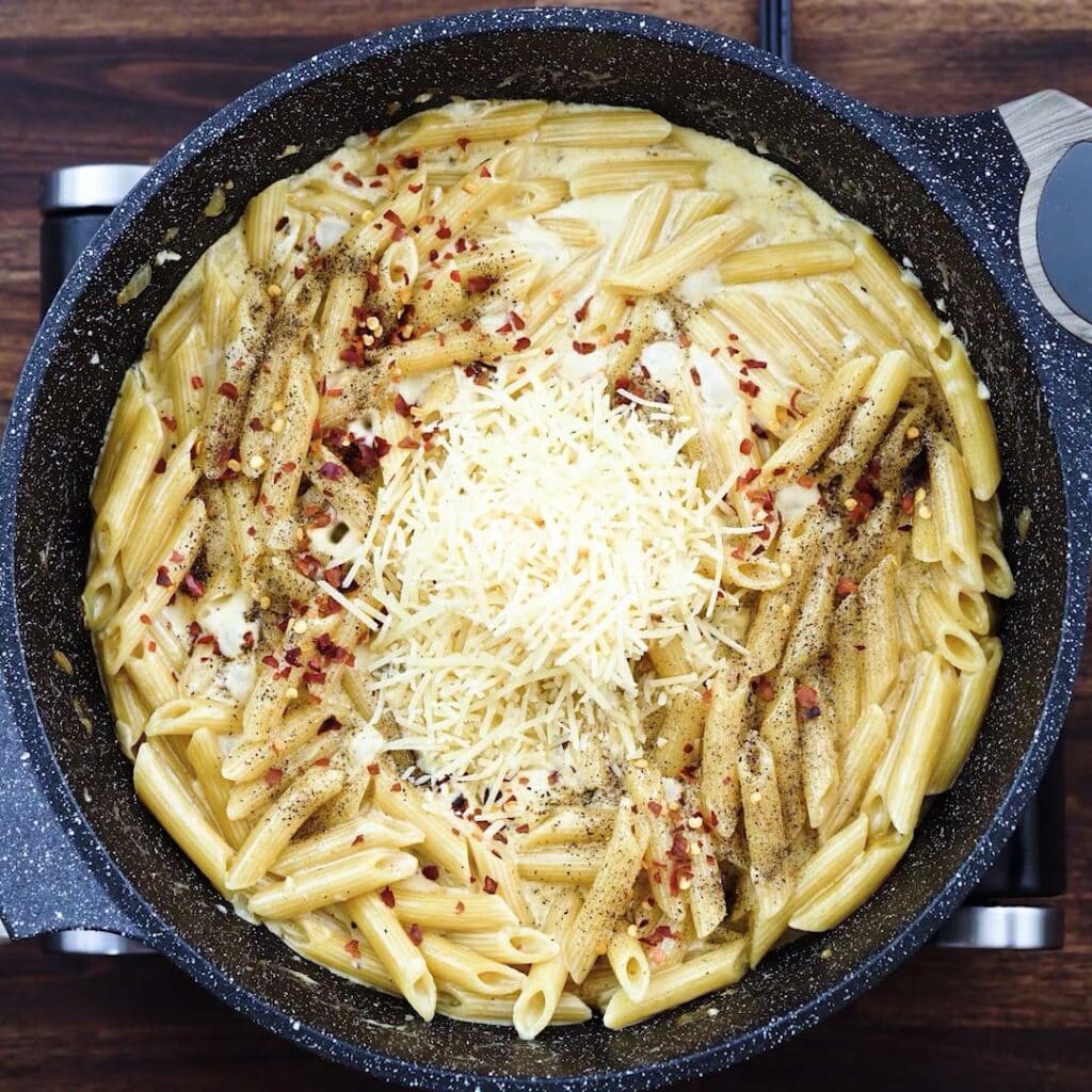 A pan with pasta, parmesan cheese, and basic seasonings.