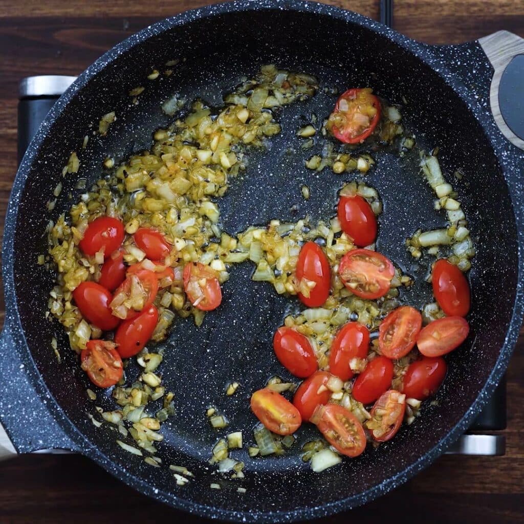Aromatics and cherry tomatoes in a pan.