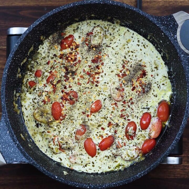 A creamy pesto sauce with aromatics in a pan.
