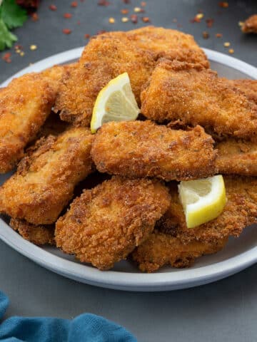 Fish Fry (Fried Fish) served in a white plate with few ingredients scattered around.