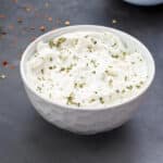 Homemade Garlic Aioli Sauce in a white bowl with few ingredients scattered around.