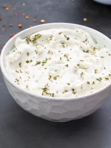 Homemade Garlic Aioli Sauce in a white bowl with few ingredients scattered around.