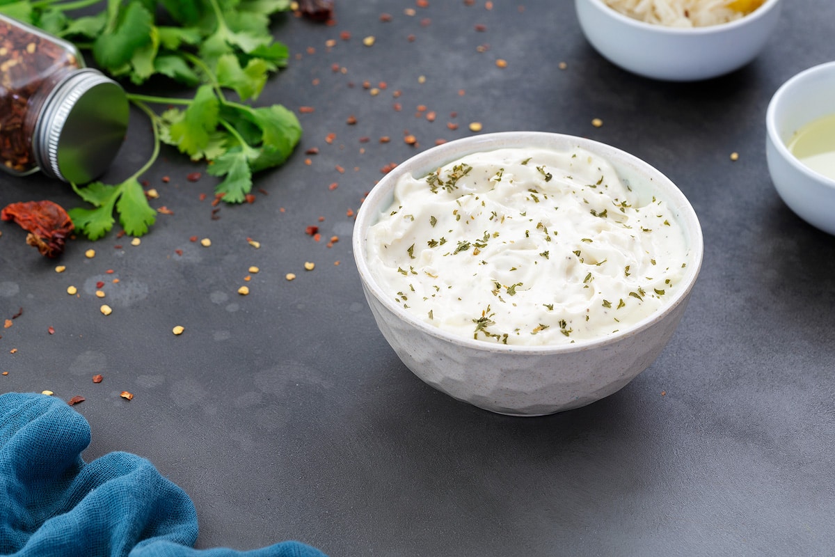 Homemade Garlic Aioli Sauce in a white bowl with few ingredients scattered around.