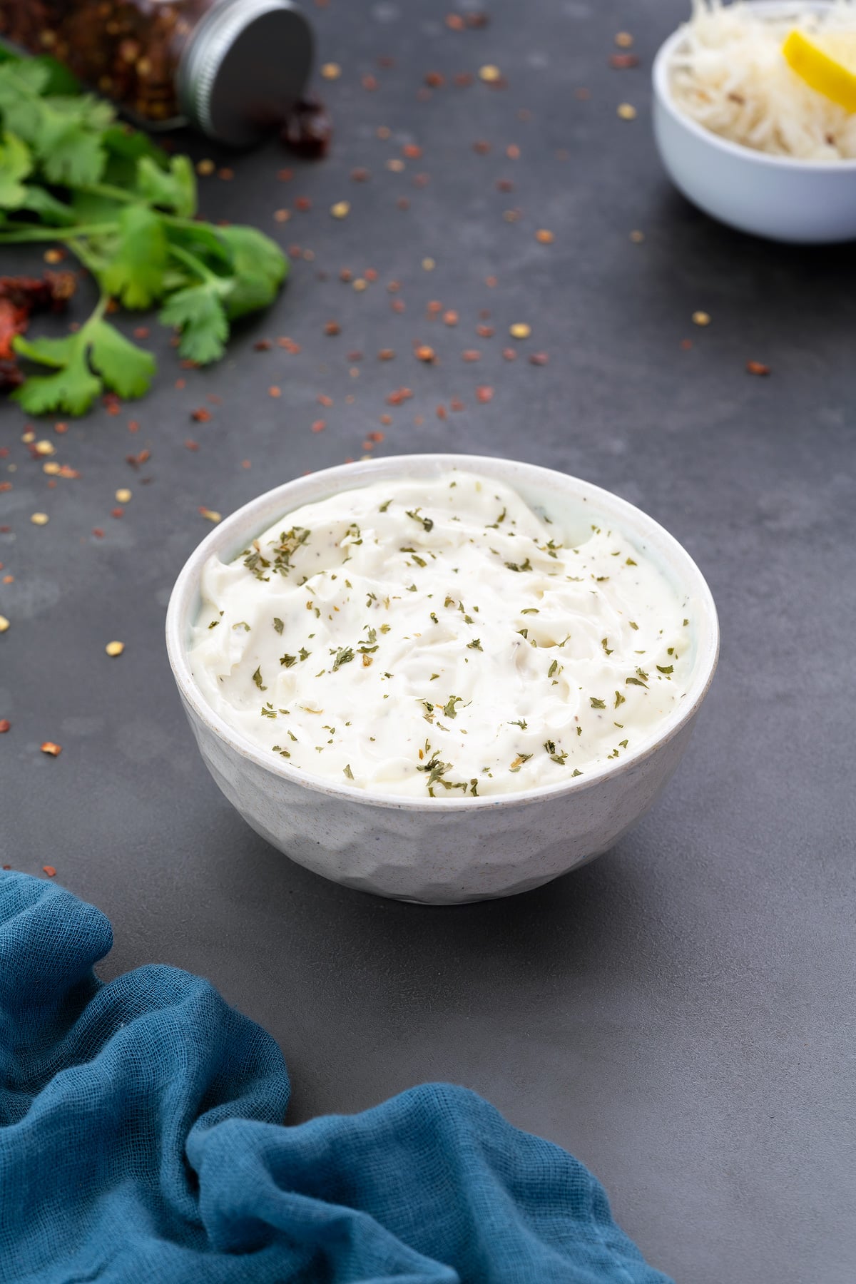 Homemade Garlic Aioli Sauce in a white bowl with few ingredients scattered around.