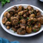 Home cooked Garlic Mushrooms in a white plate with few ingredients scattered around.