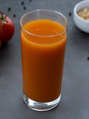 Homemade Tomato Juice in a glass with few ingredients arranged around.