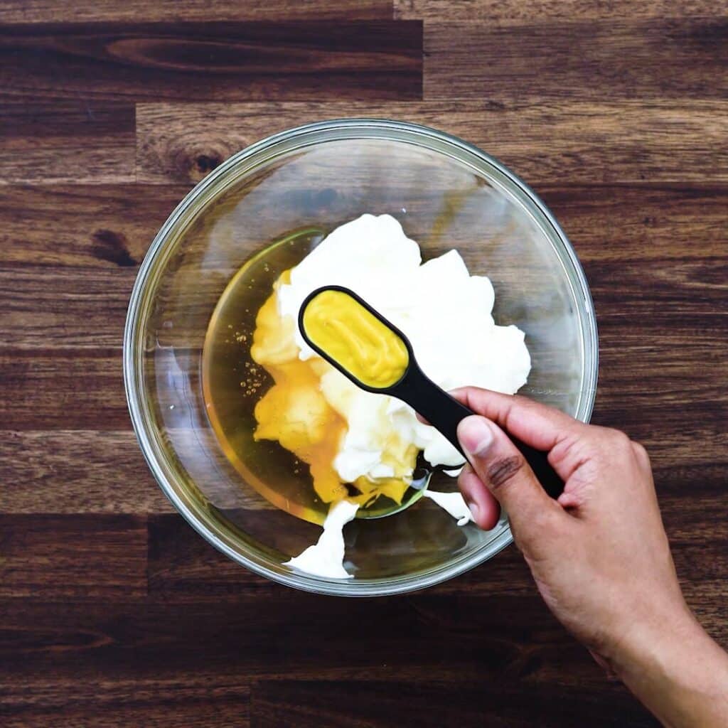 Adding yellow mustard to a bowl with mayonnaise.