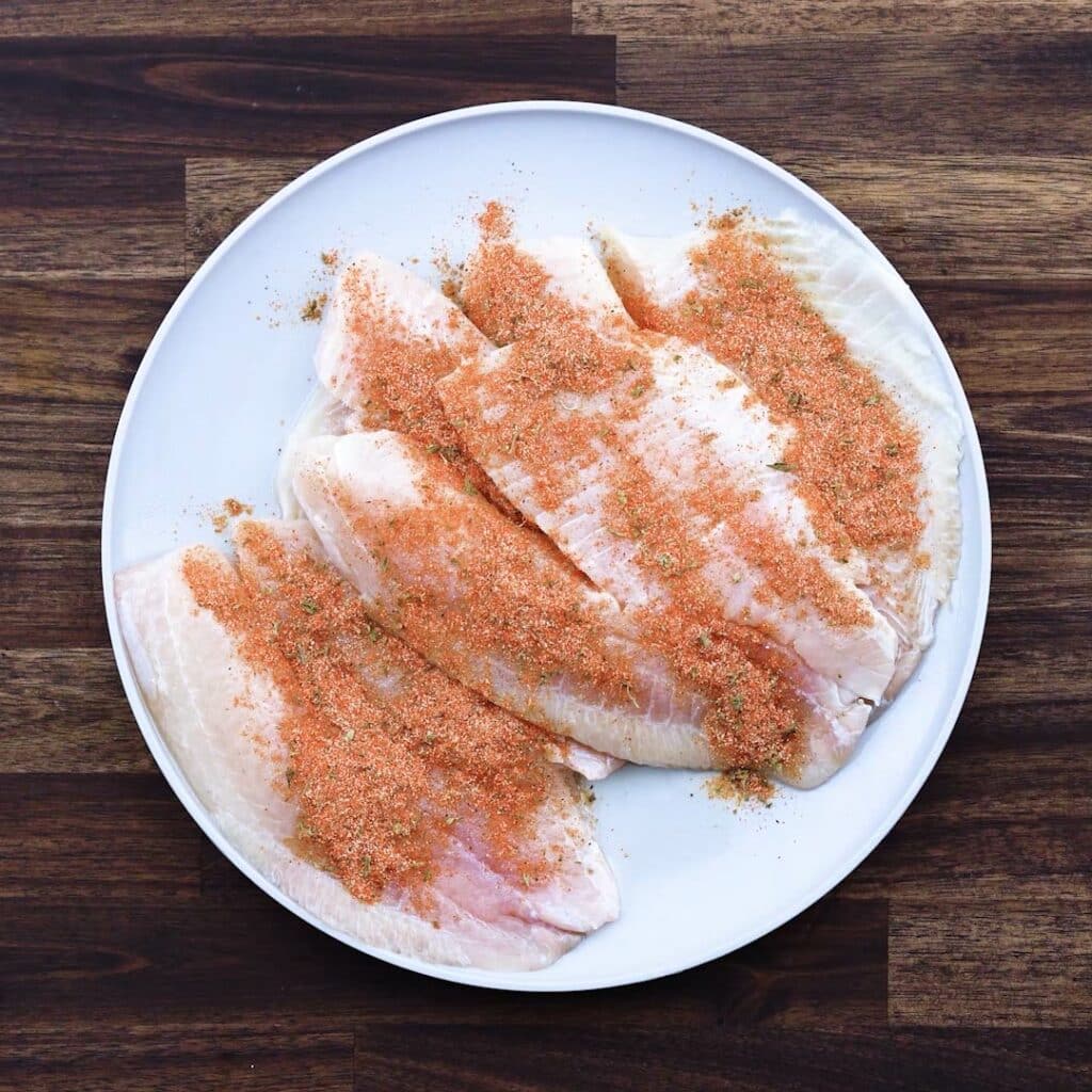 A plate with tilapia fillets seasoned with spice powders.