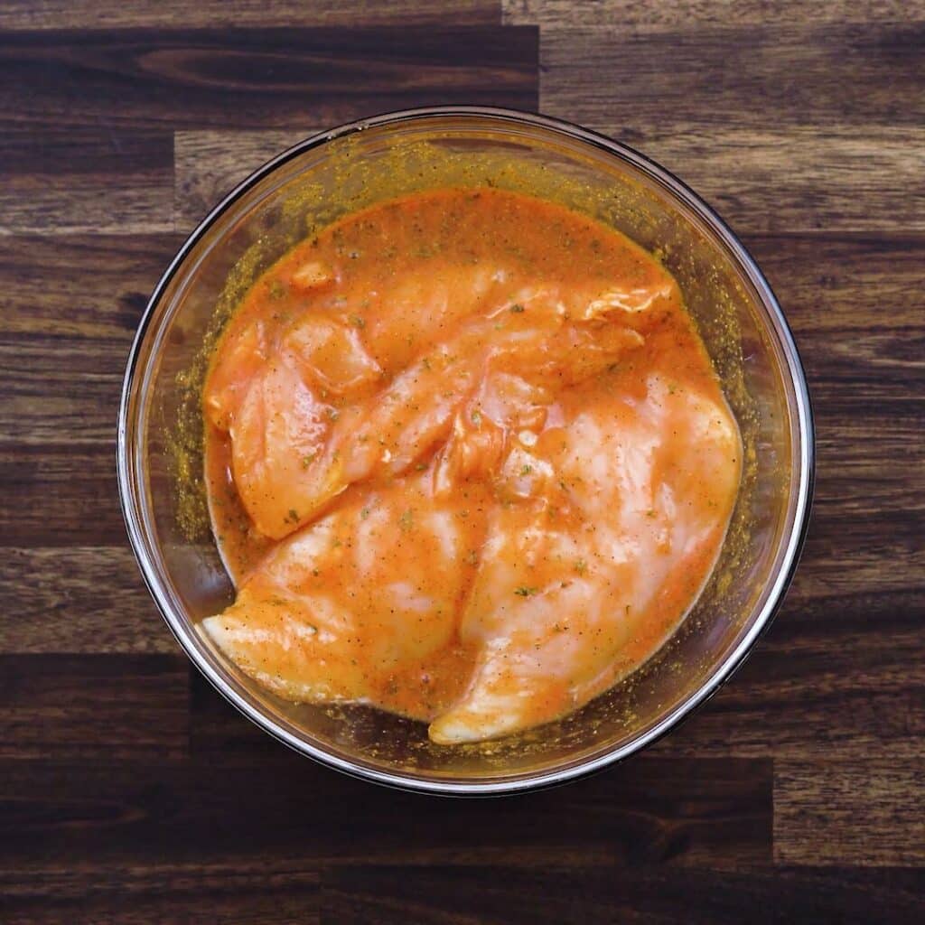 A bowl with chicken breast coated in a marinade.