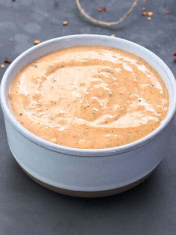 Remoulade Sauce in a white bowl with few ingredients scattered around.