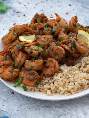 Sauteed Shrimp dish on a white plate with brown rice and garnish.