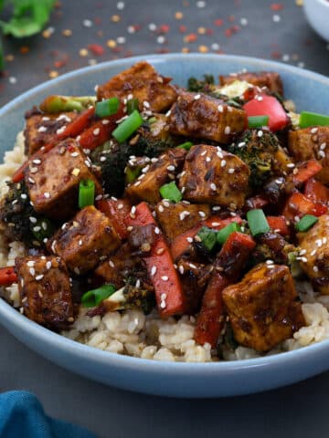 Tofu Stir Fry in a light blue bowl with few ingredients scattered around.