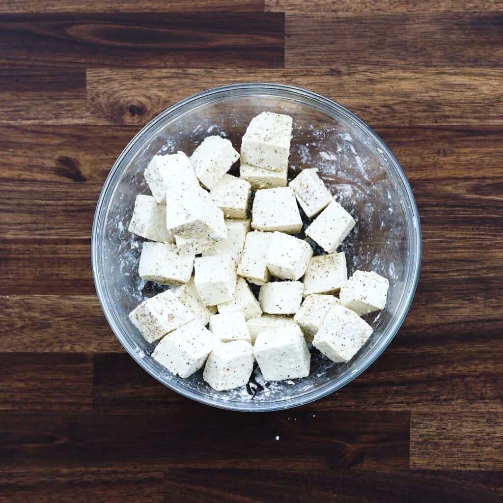 A bowl with tofu that is coated with seasonings and flour.