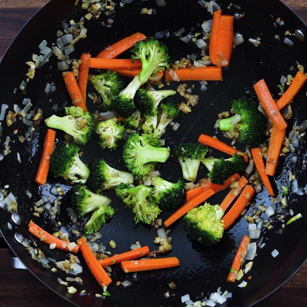 A wok with veggies and aromatics.