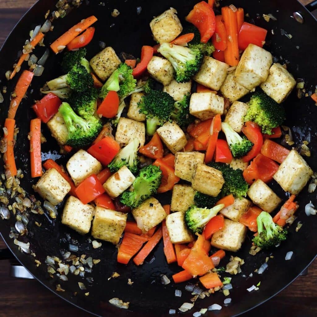 A wok with veggies, tofu and aromatics.
