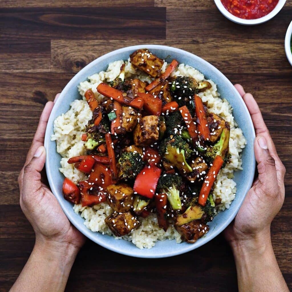 Serving the Tofu Stir Fry over rice in a serving bowl.