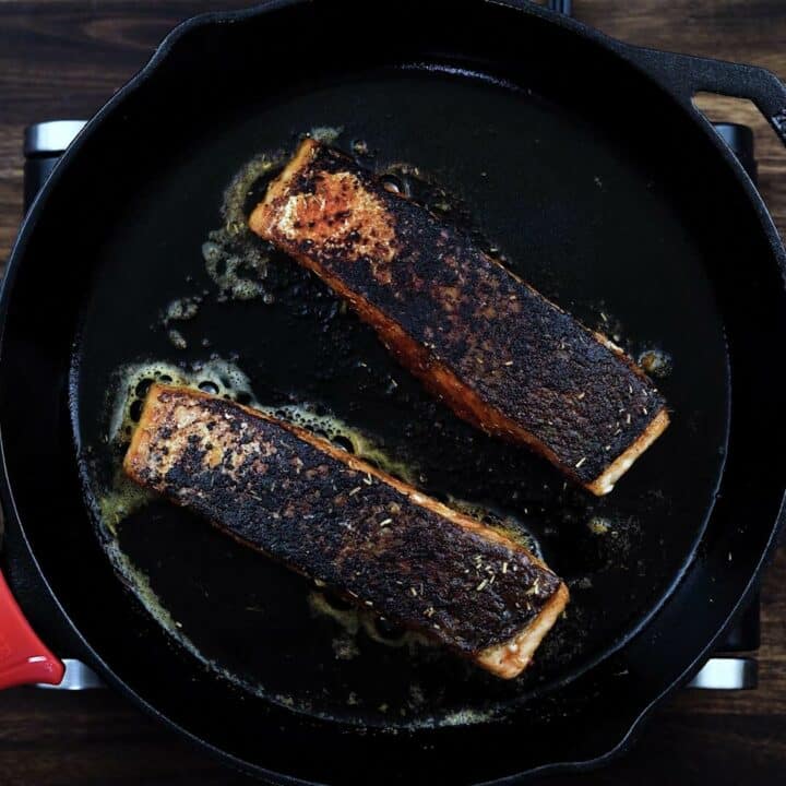 Salmon fillets frying in a cast iron facing skin side up.