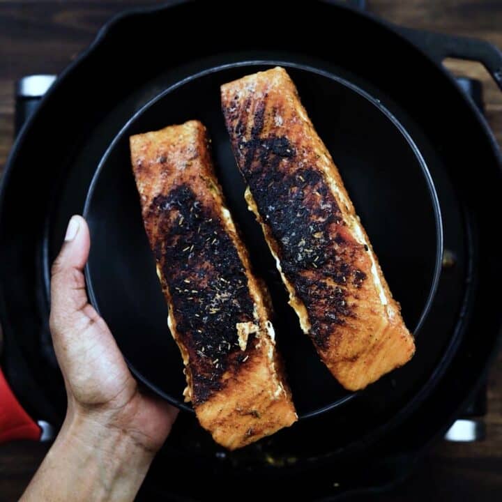 Perfectly cooked blackened salmon on a black plate.