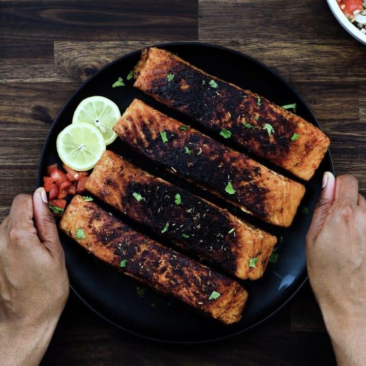 Serving Blackened Salmon with lemon slices on a black plate.