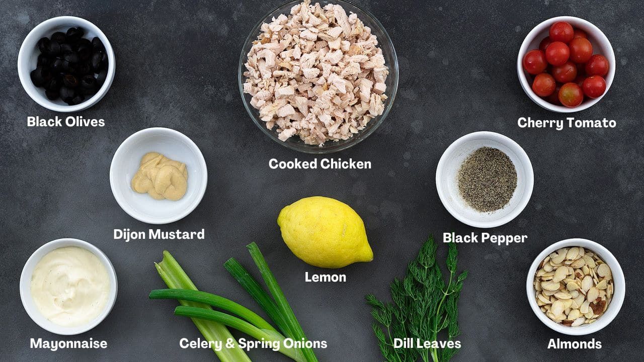 Chicken Salad recipe Ingredients including rotisserie chicken, greens and almond arranged on a grey table. Some of them are in white cups and a glass bowl.