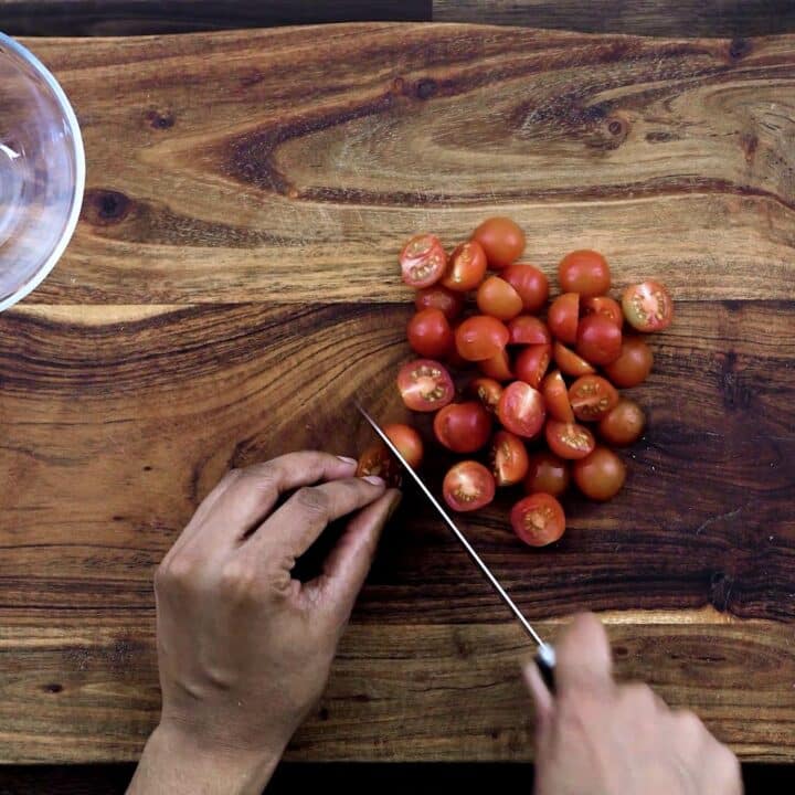 Slicing the cherry tomatoes in half using a knife.