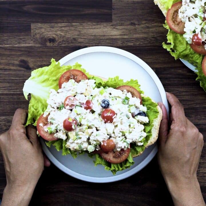 Serving creamy chicken salad over a bread with lettuce, and tomato slices.