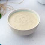 Homemade Coleslaw Salad Dressing in a white bowl placed on a white table with few ingredients around.
