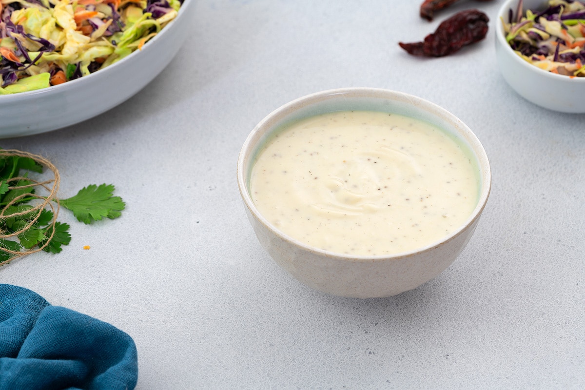 Homemade Coleslaw Salad Dressing in a white bowl placed on a white table with few ingredients around.