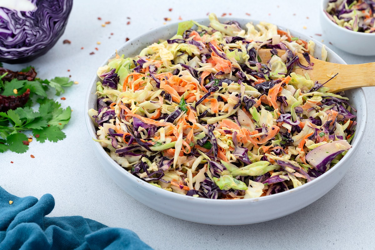 Fresh Coleslaw Salad in a white bowl with few ingredients placed around.