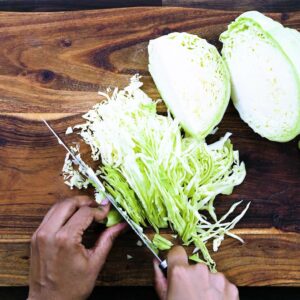 Shredding the green cabbage using knife on cutting board.