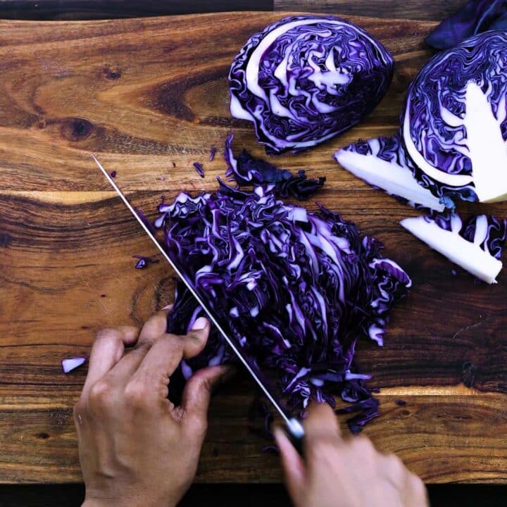 Shredding the purple cabbage using knife on cutting board.