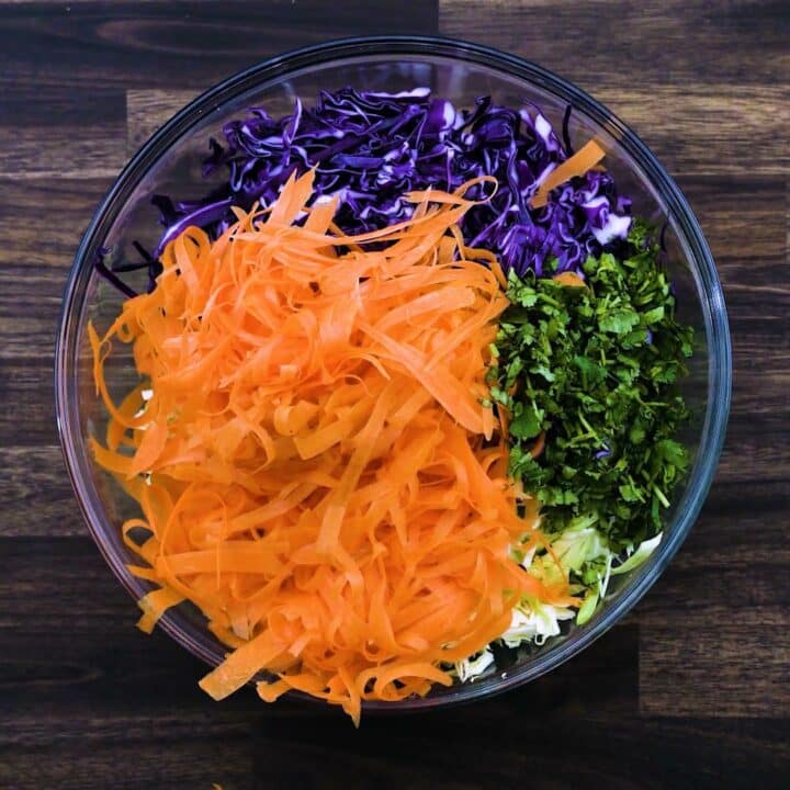 A bowl with shredded cabbages , carrots and cilantro leaves.